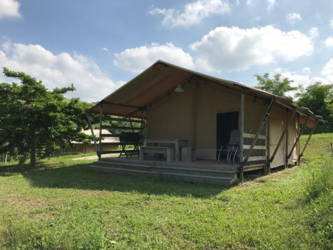 Tienda tipo safari con porche en entorno verde y soleado en Camping Podere sei Poorte, Marche, Italia.