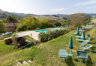 Outdoor pool with sun loungers and green umbrellas at Camping Podere sei Poorte in Marche, Italy.