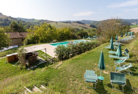 Schwimmbad mit Sonnenliegen und grünen Sonnenschirmen im Camping Podere sei Poorte, Marken, Italien.
