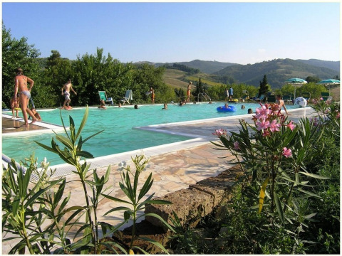 Vacacionistas disfrutan de la piscina y las vistas a las colinas en Camping Podere sei Poorte, Marche, Italia.