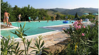 Vakantiegangers ontspannen aan het zwembad met heuvelzicht op Camping Podere sei Poorte, Marche, Italië.