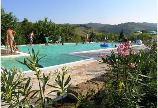 Vacacionistas disfrutan de la piscina y las vistas a las colinas en Camping Podere sei Poorte, Marche, Italia.