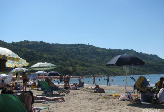 Beach scene at Camping Podere sei Poorte in Marche, Italy, with visitors relaxing under umbrellas and green hills.