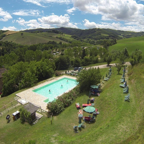 Aerial view of the pool and sunbeds at Camping Podere sei Poorte, surrounded by hills in Marche, Italy.
