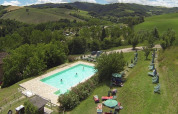 Luftfoto af swimmingpool og liggestole på Camping Podere sei Poorte, omgivet af bakker i Marche, Italien.