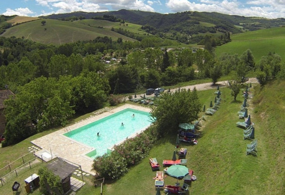 Luftfoto af swimmingpool og liggestole på Camping Podere sei Poorte, omgivet af bakker i Marche, Italien.