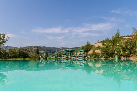 Outdoor pool with sun loungers and umbrellas at Camping Podere sei Poorte, Marche, Italy, scenic hill views.