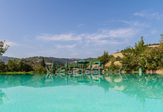 Udendørs pool med liggestole og parasoller på Camping Podere sei Poorte i Marche, Italien, omgivet af bakker.