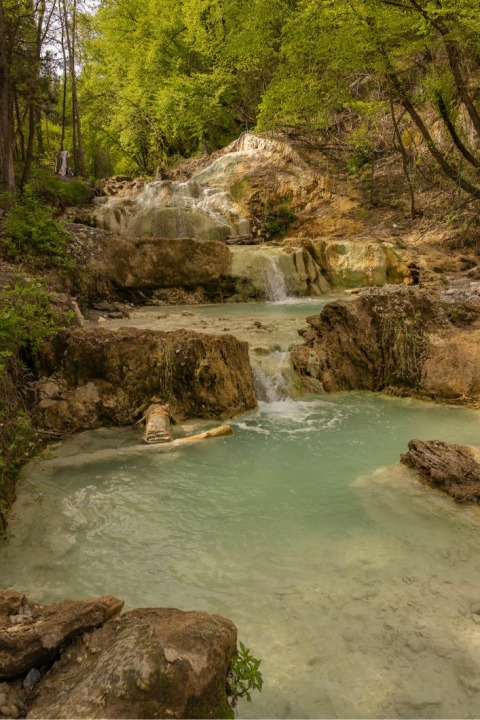Piccola cascata che scende in pozze turchesi circondate dal verde vicino a Monteciccardo, Marche, Italia.