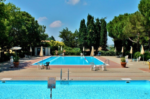Outdoor swimming pools with chairs and umbrellas at Camping Mar y Sierra holiday park in Marche, Italy.