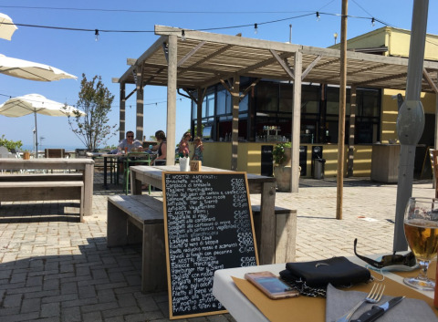 Zona de restaurante al aire libre en Camping Mar y Sierra en Marche, Italia, con un menú en pizarra visible.
