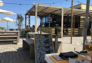 Outdoor restaurant area at Camping Mar y Sierra in Marche, Italy, with a handwritten menu chalkboard visible.