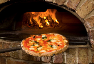 En lækker pizza bliver bagt i en traditionel stenovn med brændende ild på Camping Mar y Sierra i Marche, Italien.
