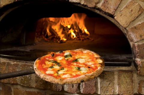 Eine köstliche Pizza wird im traditionellen Steinofen mit Feuer im Camping Mar y Sierra in Marche, Italien gebacken.