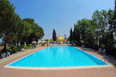 Outdoor swimming pool at Camping Mar y Sierra, Marche, Italy, surrounded by trees and yellow lodges.