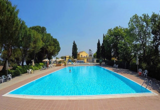 Outdoor swimming pool at Camping Mar y Sierra, Marche, Italy, surrounded by trees and yellow lodges.
