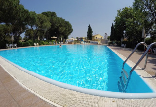 Piscina all'aperto presso il Camping Mar y Sierra, parco vacanze nelle Marche, Italia, con alberi e sedie bianche.