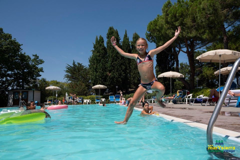 Niña feliz saltando a la piscina en Camping Mar y Sierra, un complejo vacacional en Marche, Italia.