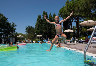 Bambina felice che salta in piscina al Camping Mar y Sierra, villaggio vacanze nelle Marche, Italia.