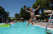 Niña feliz saltando a la piscina en Camping Mar y Sierra, un complejo vacacional en Marche, Italia.