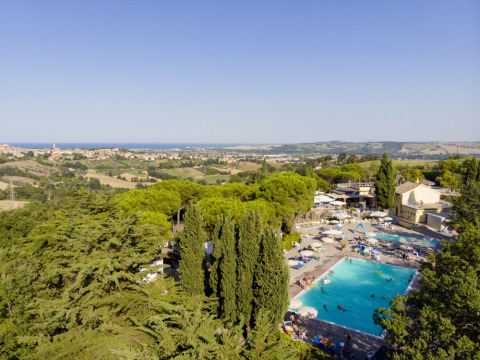 View of Camping Mar y Sierra in Marche, Italy, featuring a large pool, lush trees, and rolling hills landscape.