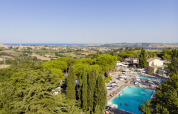 View of Camping Mar y Sierra in Marche, Italy, featuring a large pool, lush trees, and rolling hills landscape.