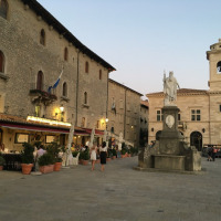 Abendliche Piazza nahe Stacciola, Marche, Italien, mit Statue, Cafés und historischen Gebäuden.