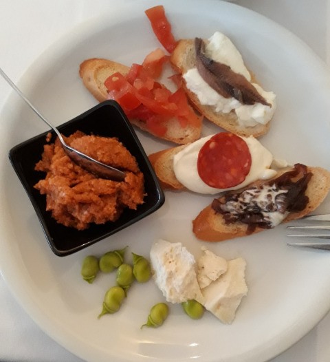 Piatto di antipasti con bruschette assortite, formaggio, fave e salsa, servito in un campeggio italiano.