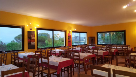 Interior de restaurante en Camping Mar y Sierra, Marche, Italia, con sillas de madera y grandes ventanales.