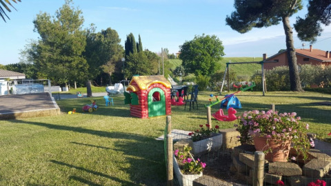 Parque infantil en Camping Mar y Sierra en Marche, Italia, con juegos, césped y flores alrededor.