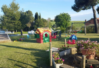 Legeplads i Camping Mar y Sierra feriepark i Marche, Italien, med legeredskaber og grønne omgivelser.
