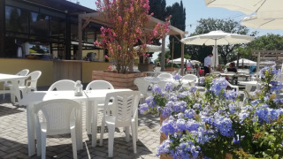Außencafé im Camping Mar y Sierra, Marche, Italien, mit weißen Sonnenschirmen und Blumen.
