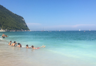 People relaxing on the sandy beach near Stacciola, Marche, Italy, with turquoise water and green hills.