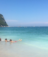 Menschen entspannen am Strand und im klaren Wasser nahe Stacciola, Marche, Italien, mit bewaldeten Hügeln.