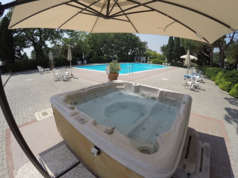 Jacuzzi y piscina al aire libre en Camping Mar y Sierra, rodeados de sillas, sombrillas y vegetación.