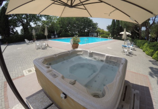 Whirlpool und Pool im Freien bei Camping Mar y Sierra, umgeben von Stühlen, Sonnenschirmen und Bäumen.