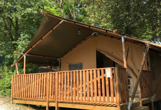 Tienda safari con terraza y baños privados en Camping Mar y Sierra, Italia, rodeada de árboles verdes.