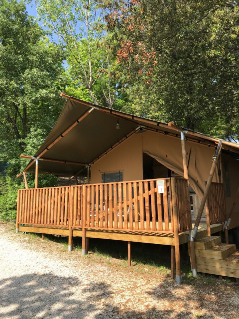 Tienda safari con terraza y baños privados en Camping Mar y Sierra, Italia, rodeada de árboles verdes.