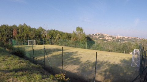 Vista de un campo de fútbol vallado rodeado de naturaleza en Camping Mar y Sierra, Marche, Italia.