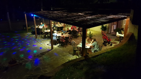 Noche en Camping Paradiso, Marche, Italia, con huéspedes cenando y relajándose bajo una terraza techada.