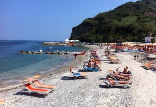 Solbadende gæster og farverige liggestole på en stenstrand ved Camping Paradiso i Marche, Italien.