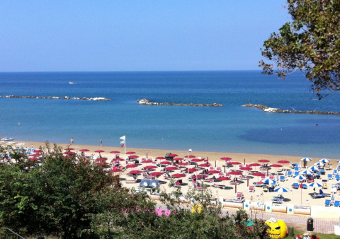 Playa cerca de Pesaro, Marcas, Italia, con sombrillas rojas, tumbonas y un mar azul tranquilo.
