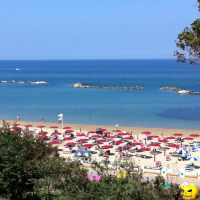 Spiaggia vicino Pesaro, Marche, Italia, con ombrelloni rossi, lettini e mare blu calmo sullo sfondo.