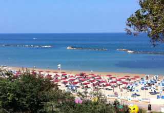 Strand nabij Pesaro, Marche, Italië, met rode parasols, ligbedden en een rustige blauwe zee.