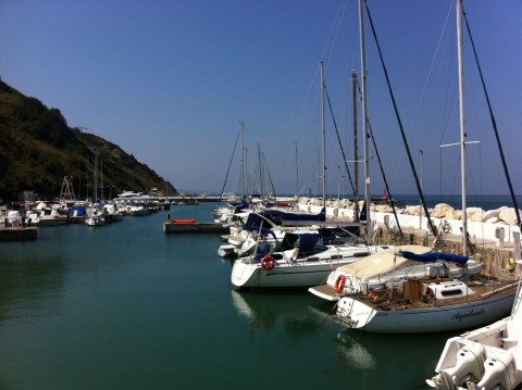 Sailboats and yachts docked in a tranquil harbor near Pesaro, Marche, Italy, on a sunny day with blue sky.
