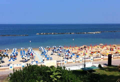 View of the beach with colorful umbrellas and loungers at Camping Paradiso holiday park in Marche, Italy.