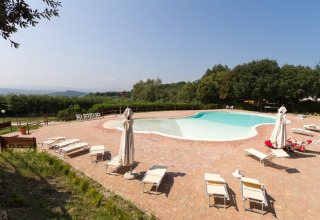Udsigt over swimmingpool og liggestole på Camping Paradiso feriepark i Marche, Italien, omgivet af natur.