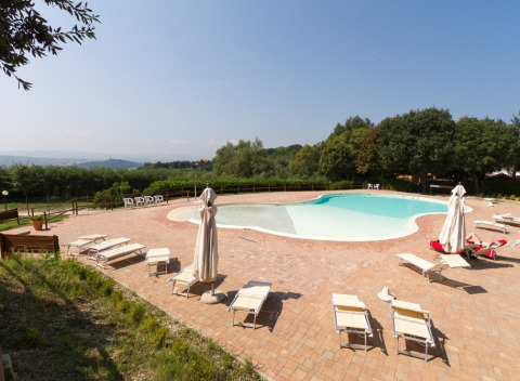 Zicht op zwembad en ligzetels in Camping Paradiso vakantiepark in Marche, Italië, omgeven door natuur.
