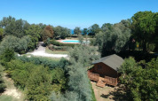 Vista aerea di Camping Paradiso nelle Marche, Italia, con piscina e una baita immersa tra gli alberi.