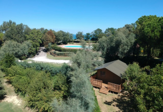 Luftfoto af Camping Paradiso feriested i Marche, Italien, med swimmingpool og hytte omgivet af træer.